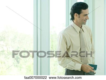 Businessman standing in front of window, smiling View Large Photo Image Stock Image - Businessman standing in front of window, smiling. Fotosearch