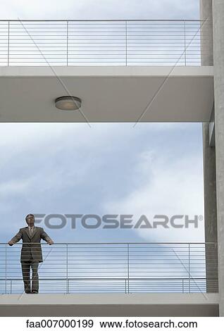 Businessman standing on walkway with hands on railing, looking into distance View Large Photo Image Stock Photo - Businessman standing on walkway with hands on railing, looking into distance. Fotosearch