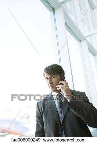 Stock Photo - Businessman using cell phone in airport. Fotosearch