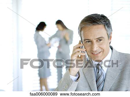 Businessman using cell phone, colleagues in background View Large Photo Image Stock Photo - Businessman using cell phone, colleagues in background. Fotosearch