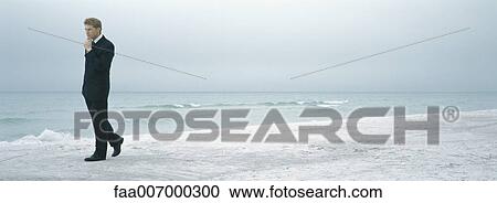 Stock Image - Businessman walking on beach. Fotosearch