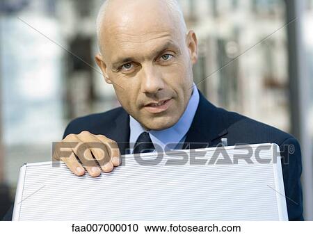 Stock Image - Businessman with hand on briefcase, looking at camera. Fotosearch