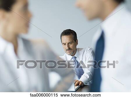 Businessman working at desk, colleagues blurred in foreground View Large Photo Image Stock Photography - Businessman working at desk, colleagues blurred in foreground. Fotosearch