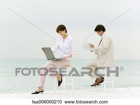 Businesspeople sitting on stools on beach, one using laptop, another reading newspaper View Large Photo Image Stock Image - Businesspeople sitting on stools on beach, one using laptop, another reading newspaper. Fotosearch