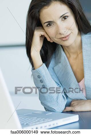 Stock Photo - Businesswoman next to laptop, smiling at camera, portrait. Fotosearch