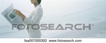 Stock Image - Businesswoman reading newspaper on beach, cropped. Fotosearch