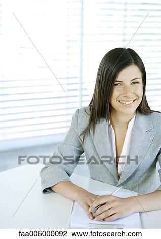 Businesswoman sitting at desk with documents, smiling View Large Photo Image Stock Image - Businesswoman sitting at desk with documents, smiling. Fotosearch
