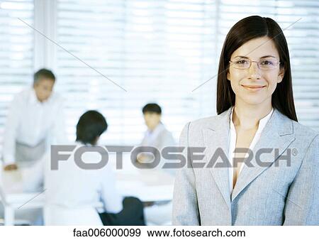 Businesswoman smiling at camera, people working in office in background View Large Photo Image Stock Photo - Businesswoman smiling at camera, people working in office in background. Fotosearch