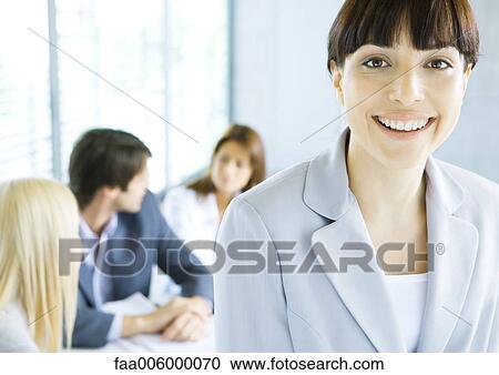 Businesswoman smiling at camera, meeting in background View Large Photo Image Stock Image - Businesswoman smiling at camera, meeting in background. Fotosearch