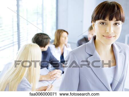 Businesswoman smiling at camera, meeting in background View Large Photo Image Stock Image - Businesswoman smiling at camera, meeting in background. Fotosearch