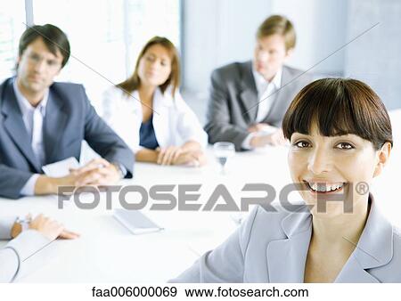 Businesswoman smiling at camera, meeting in background View Large Photo Image Stock Photo - Businesswoman smiling at camera, meeting in background. Fotosearch