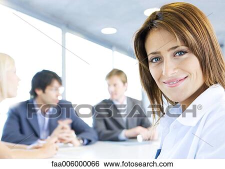 Businesswoman smiling at camera, meeting in background View Large Photo Image Stock Photograph - Businesswoman smiling at camera, meeting in background. Fotosearch