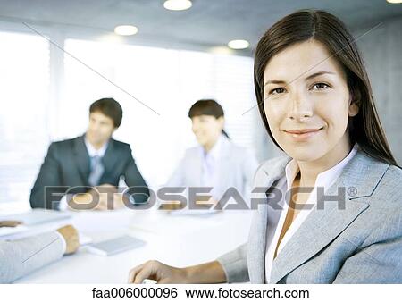 Businesswoman smiling at camera, meeting in background View Large Photo Image Stock Photograph - Businesswoman smiling at camera, meeting in background. Fotosearch