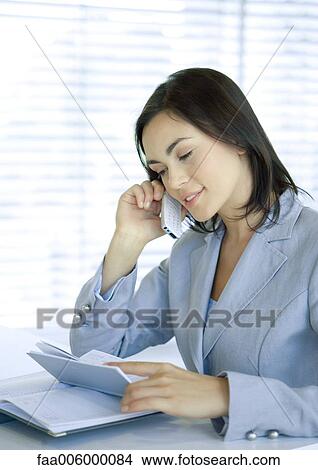 Businesswoman using cell phone and looking at agenda View Large Photo Image Picture - Businesswoman using cell phone and looking at agenda. Fotosearch