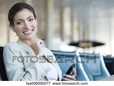 Businesswoman using electronic organizer in airport lounge area, smiling at camera View Large Photo Image Stock Photo - Businesswoman using electronic organizer in airport lounge area, smiling at camera. Fotosearch