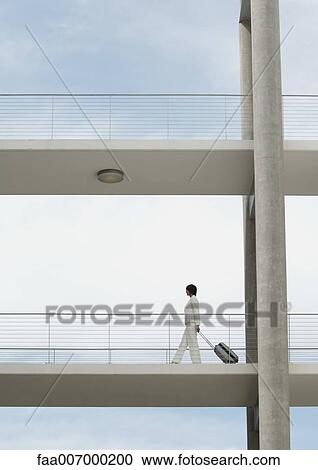 Businesswoman walking across walkway, pulling suitcase View Large Photo Image Stock Image - Businesswoman walking across walkway, pulling suitcase. Fotosearch