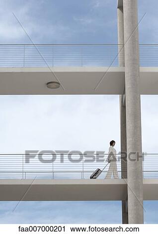 Businesswoman walking across walkway, pulling suitcase View Large Photo Image Stock Image - Businesswoman walking across walkway, pulling suitcase. Fotosearch