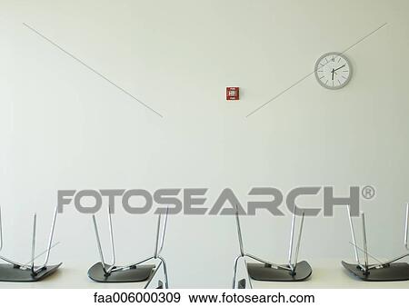 Chairs upside down on tables and clock on wall View Large Photo Image Stock Photo - Chairs upside down on tables and clock on wall. Fotosearch