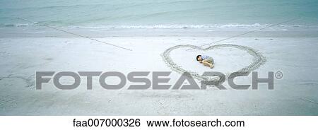 Stock Photograph - Child curled up inside heart shape on beach. Fotosearch