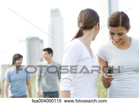 College campus, one woman looking at cell phone while another woman looks over shoulder at male friends View Large Photo Image Stock Photography - College campus, one woman looking at cell phone while another woman looks over shoulder at male friends. Fotosearch