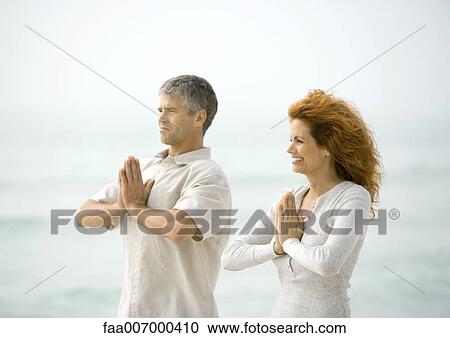 Stock Image - Couple doing relaxation exercises together on beach. Fotosearch