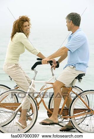 Couple face to face on bikes, on beach View Large Photo Image Stock Photo - Couple face to face on bikes, on beach. Fotosearch