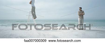 Couple on beach, woman standing on ladder, looking away from man, both crossing arms View Large Photo Image Stock Photo - Couple on beach, woman standing on ladder, looking away from man, both crossing arms. Fotosearch