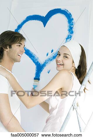 Stock Photo - Couple painting, woman drawing heart on wall. Fotosearch