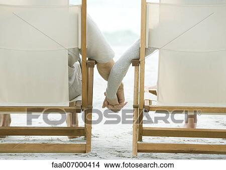 Couple sitting in beach chairs, holding hands, rear view View Large Photo Image Picture - Couple sitting in beach chairs, holding hands, rear view. Fotosearch