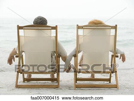 Couple sitting in beach chairs, holding hands, rear view View Large Photo Image Stock Photography - Couple sitting in beach chairs, holding hands, rear view. Fotosearch