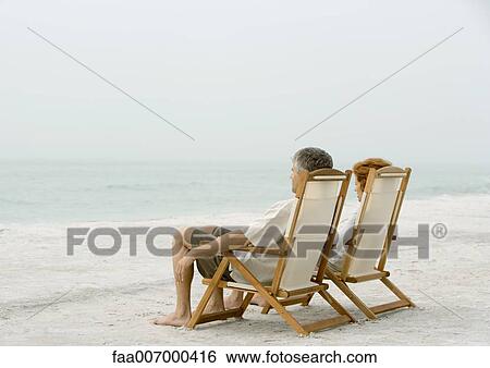 Stock Photograph - Couple sitting in beach chairs, looking at view. Fotosearch