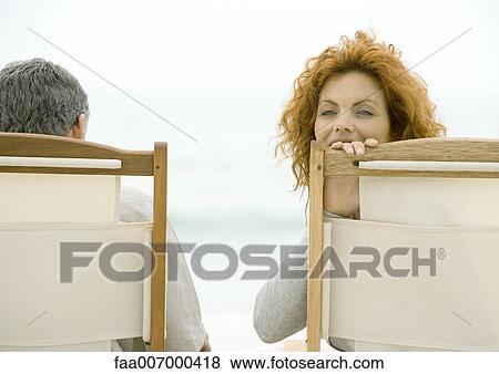 Stock Photo - Couple sitting in beach chairs, woman turning around, looking at camera. Fotosearch