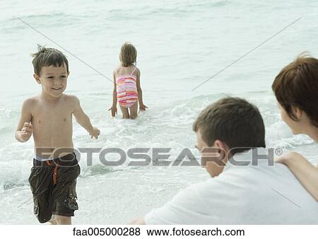 Family at the beach, boy running out of water towards parents View Large Photo Image Stock Photo - Family at the beach, boy running out of water towards parents. Fotosearch