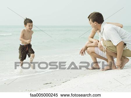Stock Photography - Family at the beach, boy running out of water towards parents. Fotosearch