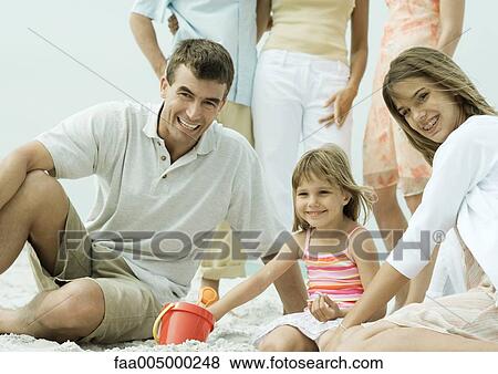 Stock Photo - Family at the beach, man sitting on sand with two daughters. Fotosearch