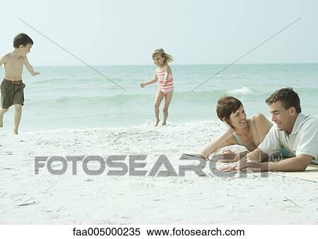 Family at the beach, parents lying on sand while children play View Large Photo Image Stock Photography - Family at the beach, parents lying on sand while children play. Fotosearch