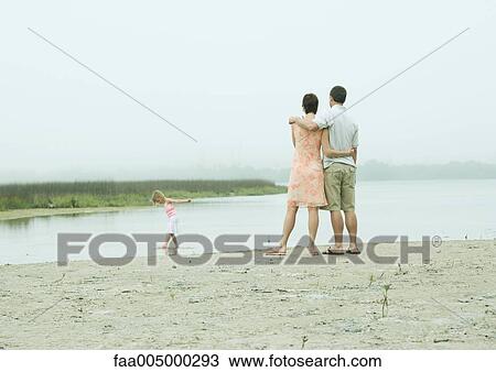 Family at the beach, parents watching little girl play in water View Large Photo Image Stock Image - Family at the beach, parents watching little girl play in water. Fotosearch