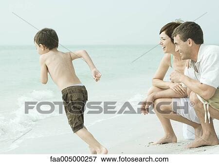 Family at the beach, parents watching son run towards water View Large Photo Image Stock Photo - Family at the beach, parents watching son run towards water. Fotosearch