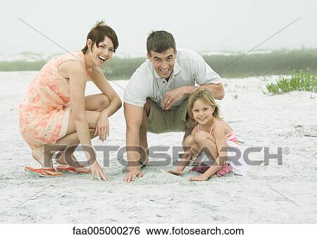 Stock Photograph - Family at the beach, playing in the sand, smiling at camera. Fotosearch