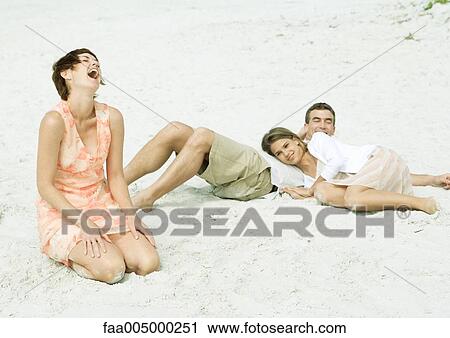 Stock Image - Family at the beach, teenage girl resting head on father's stomach while mother laughs. Fotosearch