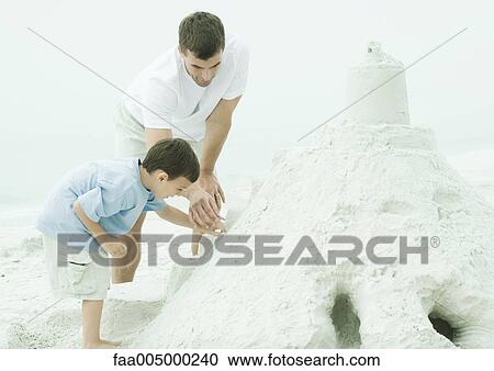 Stock Image - Father and son building sand castle at the beach. Fotosearch