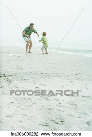 Stock Image - Father and son playing around on beach. Fotosearch