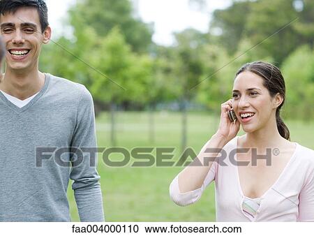 Stock Image - Friends in city park, one using cell phone. Fotosearch