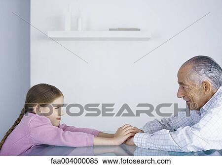 Girl and grandfather sitting across from each other at table, holding hands View Large Photo Image Stock Photography - Girl and grandfather sitting across from each other at table, holding hands. Fotosearch