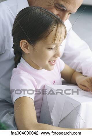 Girl holding present while grandfather looks over her shoulder View Large Photo Image Stock Image - Girl holding present while grandfather looks over her shoulder. Fotosearch