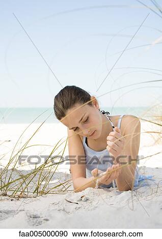 Stock Image - Girl lying on beach, letting sand run through hands. Fotosearch