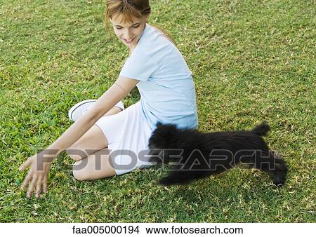 Picture - Girl sitting on grass, playing with puppy. Fotosearch