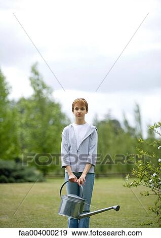 Girl standing in yard with watering can View Large Photo Image Stock Photo - Girl standing in yard with watering can. Fotosearch
