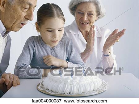 Stock Photo - Girl with grandparents, gathered around birthday cake. Fotosearch