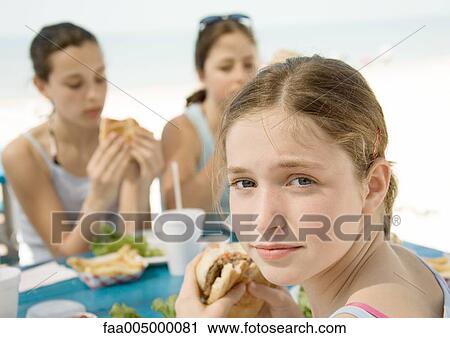 Stock Image - Girls eating hamburgers next to beach. Fotosearch